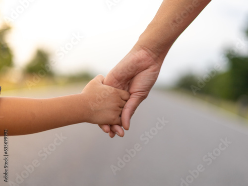 Hands of a mother and child walk hand in hand on the road. under the evening sun