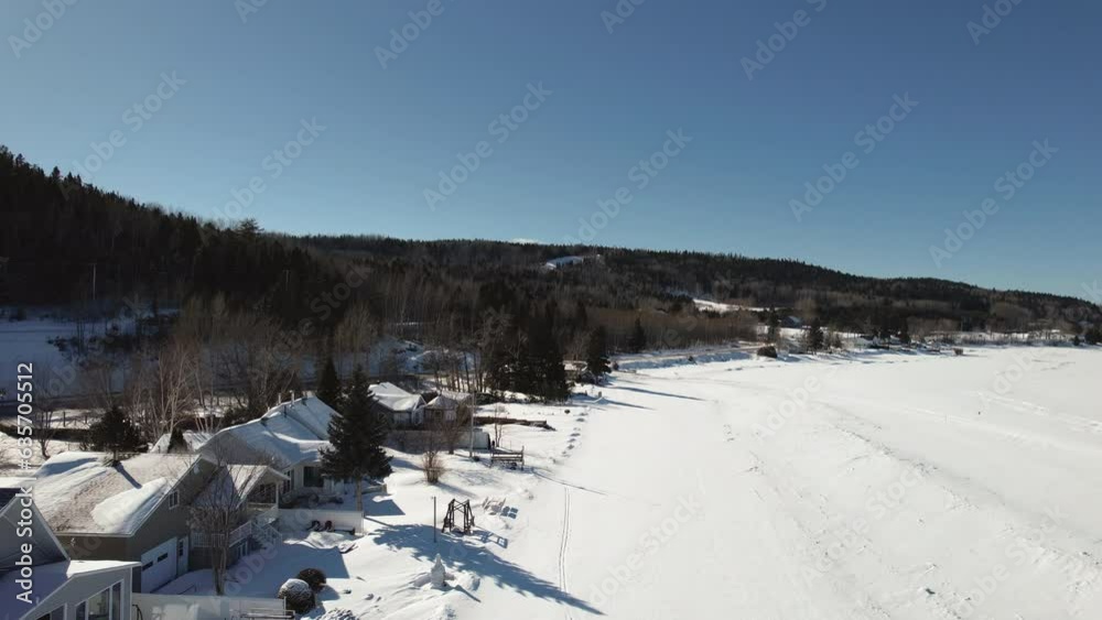 Flying drone above houses and a frozen lake during winter in canada Flying drone above houses and a frozen lake during winter in canada
