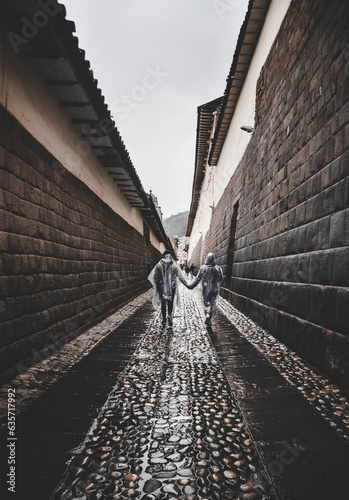 Street in Cuzco, rainy day, wet pavement, stone pathway, couple walking hand in hand in the rain.