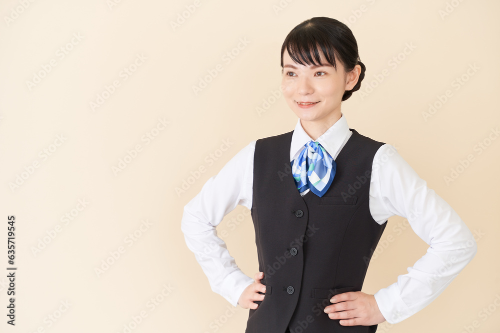腰に手を当てるベストにリボンタイの制服を着た、受付業務、事務業務の女性 腰に手を当てるベストにリボンタイの制服を着た、受付業務、事務業務の女性