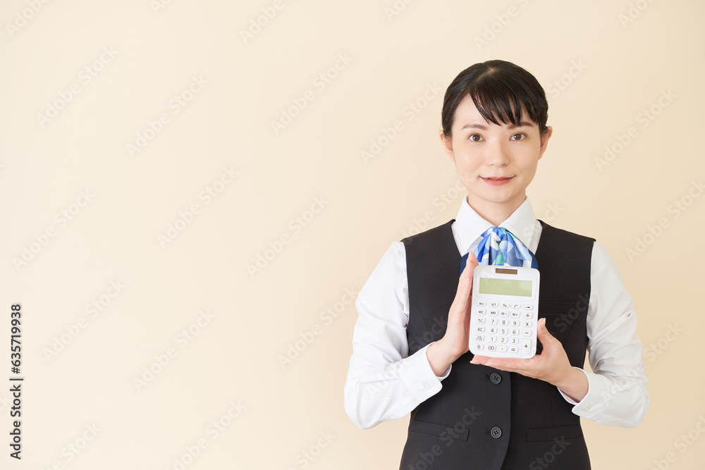 電卓をもつベストにリボンタイの制服を着た、受付業務、事務業務の女性
