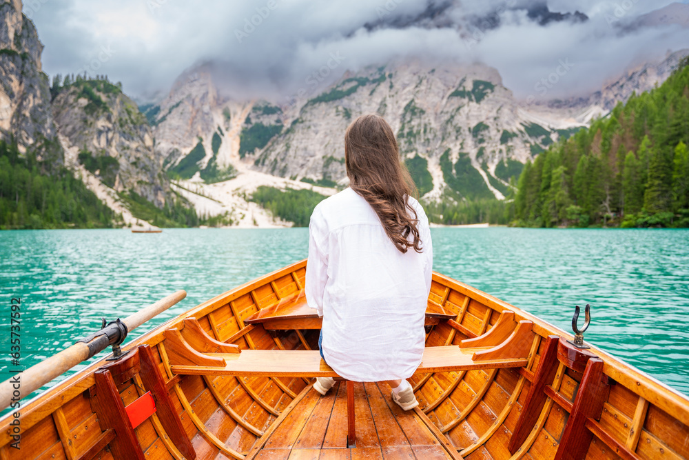 Woman sitting in big brown boat at Lago Braies lake in cloudy day, Italy. Summer vacation in Europe