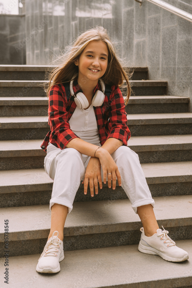 cool girl holding sitting on stairs at school, smiling and looking at camera