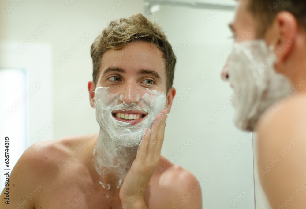 Man looking at himself in the mirror, smiling while shaving his beard. Personal hygiene and care concep