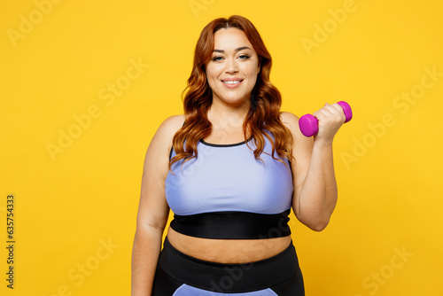 Young happy chubby overweight plus size big fat fit woman wear blue top warm up training hold in hand dumbbell look camera isolated on plain yellow background studio home gym. Workout sport concept. © ViDi Studio