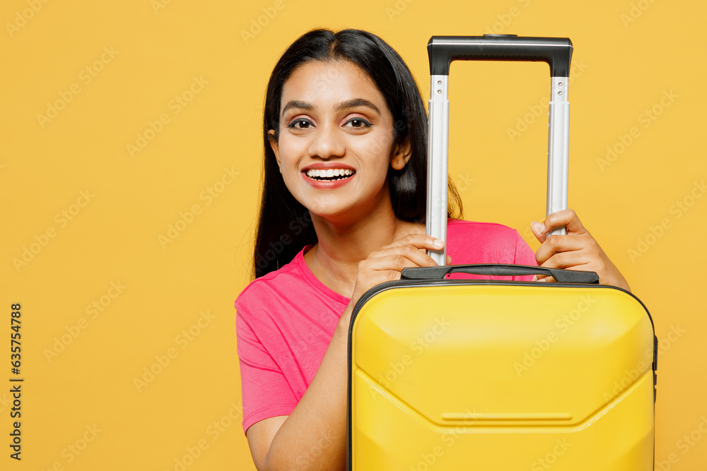 Traveler Indian woman wear summer casual clothes pink t-shirt hold suitcase isolated on plain yellow background. Tourist travel abroad in free spare time rest getaway. Air flight trip journey concept. Traveler Indian woman wear summer casual clothes pink t-shirt hold suitcase isolated on plain yellow background. Tourist travel abroad in free spare time rest getaway. Air flight trip journey concept.