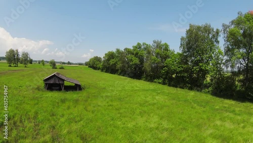 Wallpaper Mural Overflight of a green field with blue sky and white clouds. There are trees in the background and a small wooden hut Torontodigital.ca