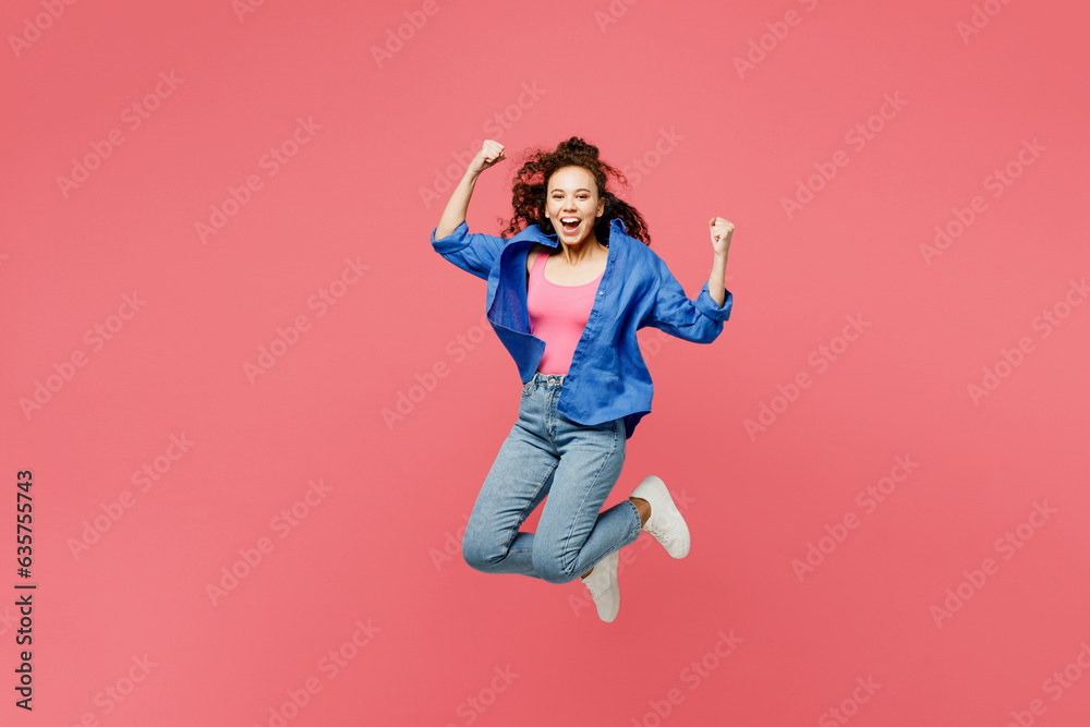 Full body happy young woman of African American ethnicity she wear blue shirt casual clothes jump high jump high do winner gesture isolated on plain pastel pink background studio. Lifestyle concept.
