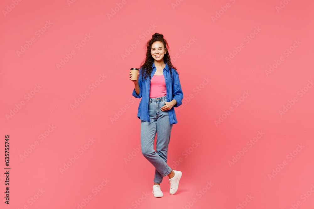 Full body young happy woman of African American ethnicity she wear blue shirt casual clothes hold takeaway delivery craft paper brown cup coffee to go isolated on plain pastel pink background studio.