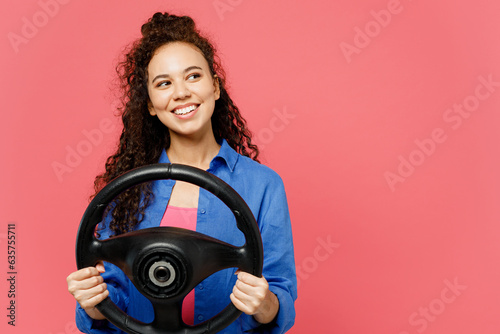 Young minded woman of African American ethnicity wear blue shirt casual clothes hold steering wheel driving car look aside on area isolated on plain pastel pink background studio. Lifestyle concept. photo