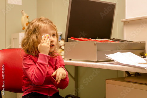 Eye exam, cute smiled little girl is reviewing eyesight. photo