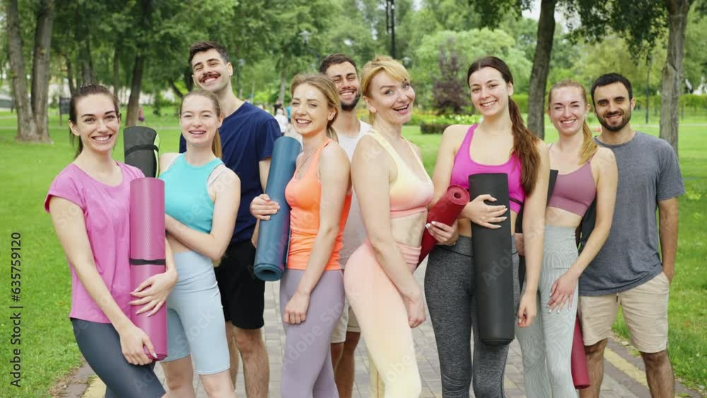Cheerful happy group of young people with yoga mats smiling to camera after fitness session. Good mood before yoga training. Outdoor sports activities in the fresh air. Health and wellness concept Cheerful happy group of young people with yoga mats smiling to camera after fitness session. Good mood before yoga training. Outdoor sports activities in the fresh air. Health and wellness concept