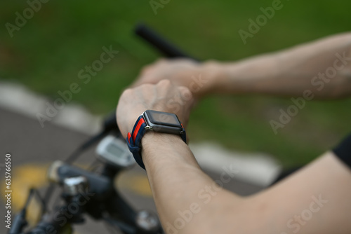 Cropped image of man cyclist sitting on his bicycle and checking sport activity progress data on smartwatch.