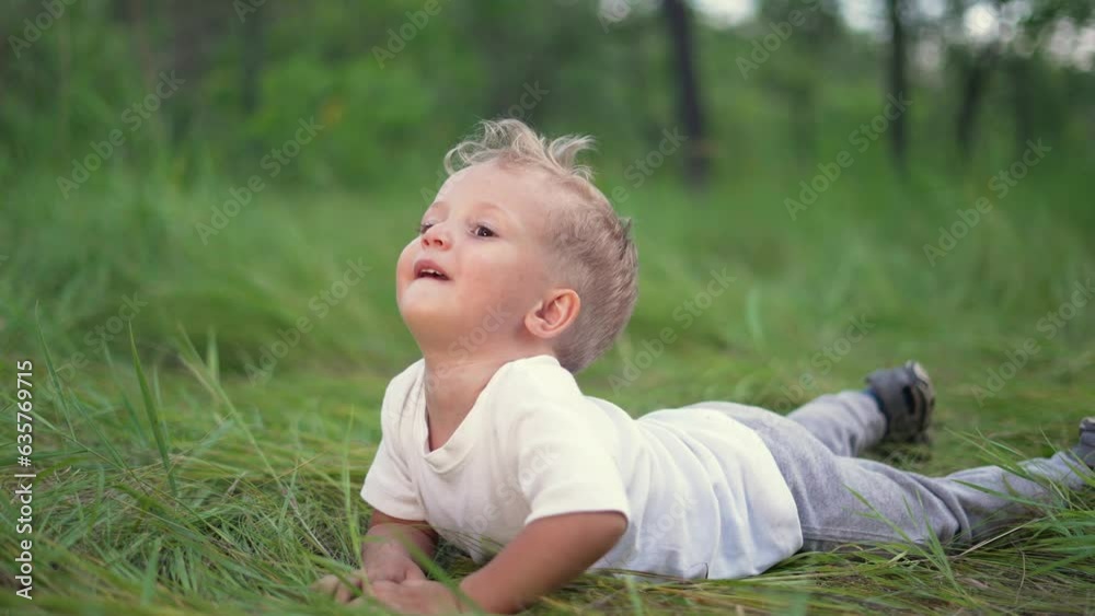 Joyful happy boy crawling in park. First steps. The boy crawls in forest park on the grass. Boy dream concept. The kid takes the first steps in the park on the green grass. Happiness and fun concept Joyful happy boy crawling in park. First steps. The boy crawls in forest park on the grass. Boy dream concept. The kid takes the first steps in the park on the green grass. Happiness and fun concept