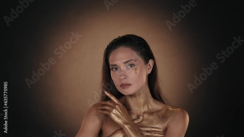 Attractive woman with shiny makeup, looking at the camera, teardrop of golden paint flowing down by her cheek photo