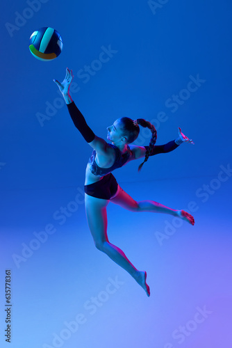 Top view of professional volleyball player, young woman in motion, hitting ball against blue studio background in neon light. Concept of professional sport, competition, health, hobby, action, ad © master1305