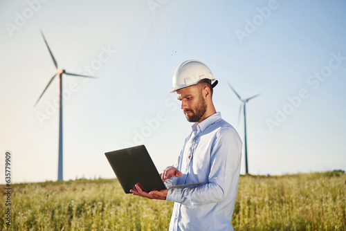 Standing and using laptop. Service engineer is on the field with windmills photo