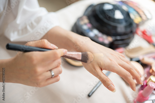 Close-up top view image of a female applying foundation to her hand with a makeup brush.