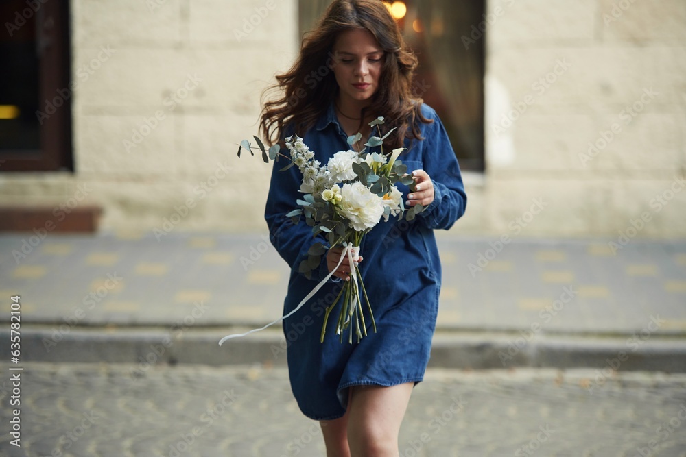 Fototapeta premium In blue clothes. Beautiful woman is with flowers in hands outdoors