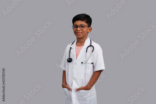 Indian Asian kid boy aged 7 to 8  wearing a doctor apron with stethoscope and standing. He had a dream to future study as Doctor. He smiled happily  Concept little Doctor
