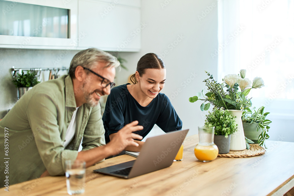 Obraz premium Happy father and daughter using a laptop, leaning on a kitchen island.