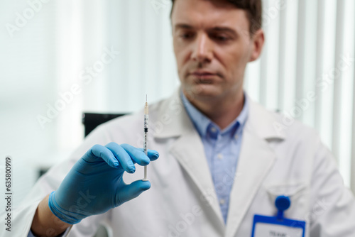 Plastic surgeon looking at syringe with anesthetic in his hand