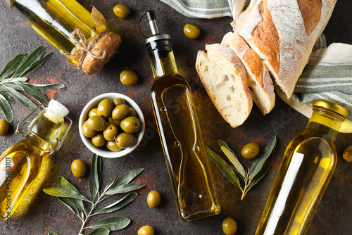 Bottles of olive oil, olives and slices of bread on gray background, top view