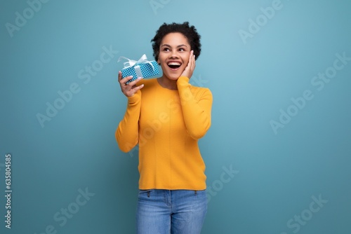 happy joyful young brunette latin female adult in yellow sweater received a gift in a box