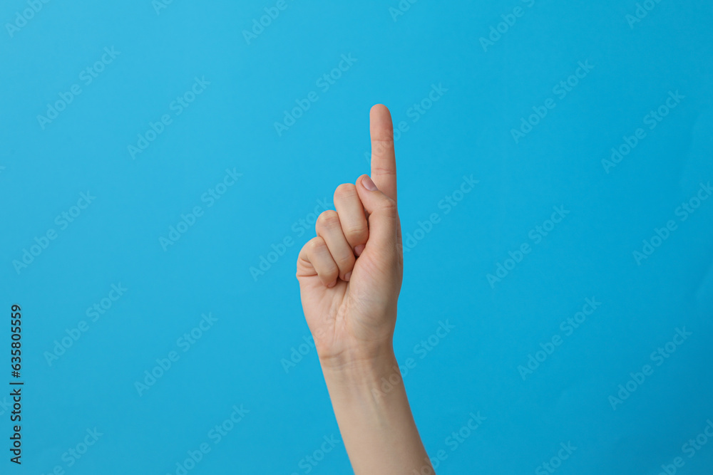Female hand showing one finger on blue background Female hand showing one finger on blue background