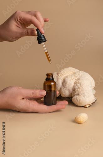 essential oil in bottle and cosmetic product in woman hand on studio beige background against beautiful lion mane mushroom