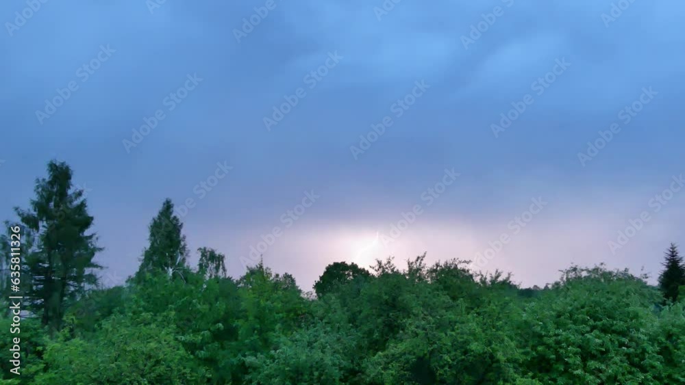 Dark blue stormy sky with lightning and flashes over green trees during thunderstorm on spring period - real time with slow motion. Topics: weather, season, natural environment, climate, meteorology Dark blue stormy sky with lightning and flashes over green trees during thunderstorm on spring period - real time with slow motion. Topics: weather, season, natural environment, climate, meteorology