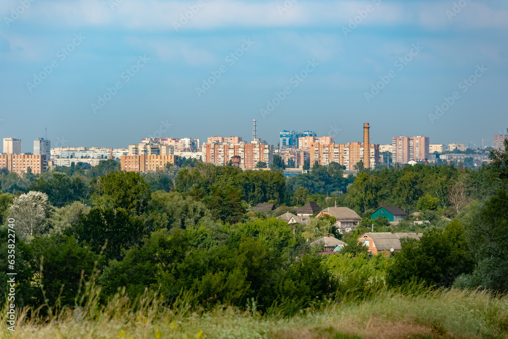 Obraz premium View of the Kharkiv on a summer sunny day. Cityscape with trees in the foreground and high-rise buildings on the horizon