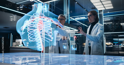 Two Bioengineers Working With Computer-Powered VFX Hologram Of Human Chest With Heart And Blood Flow In Futuristic Lab. Caucasian Man And Woman Working On Innovative Heart Attack Prevention.