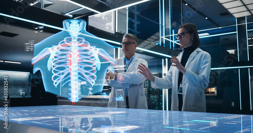 Two Bioengineers Working With Computer-Powered VFX Hologram Of Human Chest With Heart And Blood Flow In Futuristic Lab. Caucasian Man And Woman Working On Innovative Heart Attack Prevention Solution.