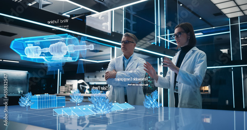 Male And Female Renewable Energy Engineers Using Futuristic Hologram of Wind Turbine Prototype In Computer Powered Laboratory. Caucasian Colleagues Controlling VFX Projection Technology With Gestures.