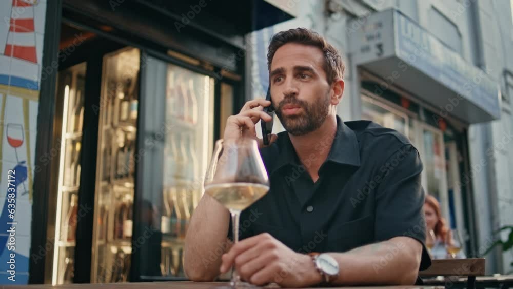 Latin macho calling mobile phone in street bar close up. Man holding wine glass