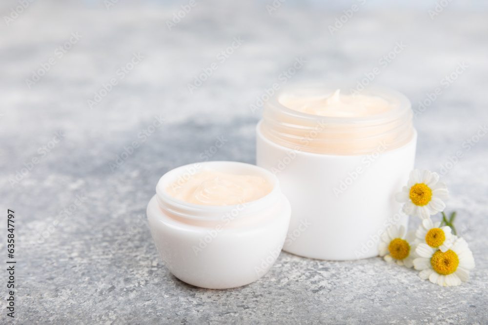 Open jar of cream for face, body and hands with chamomile flower on a blue background. Herbal dermatological cosmetic hygiene cream. Natural cosmetic product. Beauty concept. Cosmetic tube.MOCKUP Open jar of cream for face, body and hands with chamomile flower on a blue background. Herbal dermatological cosmetic hygiene cream. Natural cosmetic product. Beauty concept. Cosmetic tube.MOCKUP