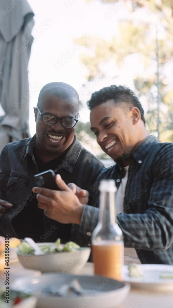 Two Men Laughing at A Cell Phone at an Outdoor lunch Two Men Laughing at A Cell Phone at an Outdoor lunch