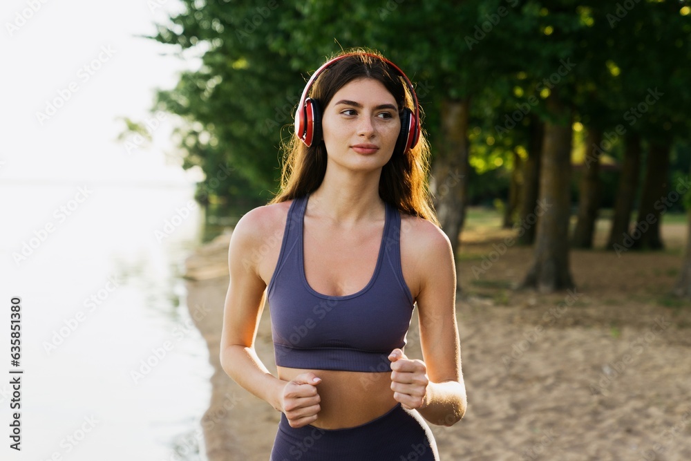 Jogging on the beach in the morning in summer. A young woman in a tracksuit and headphones trains outside. Jogging on the beach in the morning in summer. A young woman in a tracksuit and headphones trains outside.