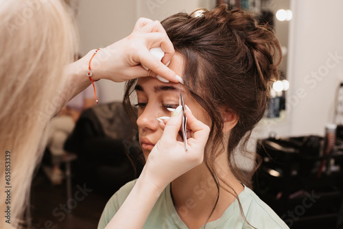 Shooting in a beauty salon. The master brow artist plucks out the hairs, giving the correct shape to the eyebrows of the model.