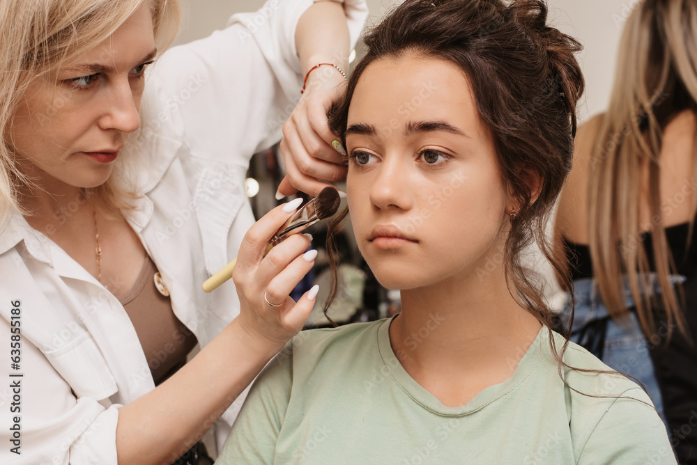 Shooting in a beauty salon. A master makeup artist applies blush, highlighter and a sculptor to the skin of a model's girl. Shooting in a beauty salon. A master makeup artist applies blush, highlighter and a sculptor to the skin of a model's girl.