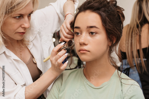 Shooting in a beauty salon. A master makeup artist applies blush, highlighter and a sculptor to the skin of a model's girl.