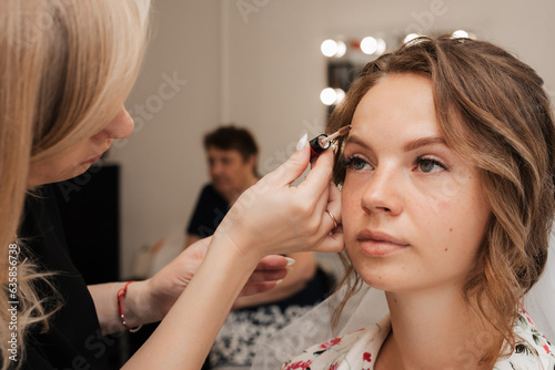 Shooting in a beauty salon. makeup artist makes a wedding makeup for a young beautiful girl.