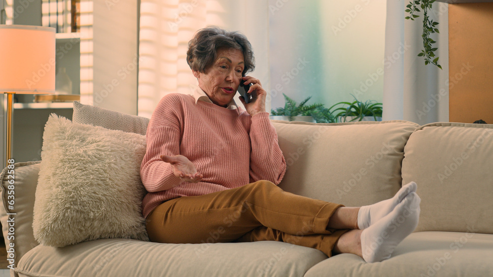 Obraz premium Caucasian mad aggressive dissatisfied old woman senior lady mature retirement granny elderly female at couch at home talk angry mobile phone call talking conflict misunderstanding quarrel smartphone