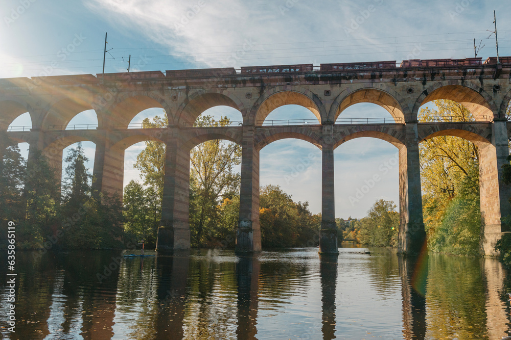 Fototapeta premium Railway Bridge with river in Bietigheim-Bissingen, Germany. Autumn. Railway viaduct over the Enz River, built in 1853 by Karl von Etzel on a sunny summer day. Bietigheim-Bissingen, Germany. Old