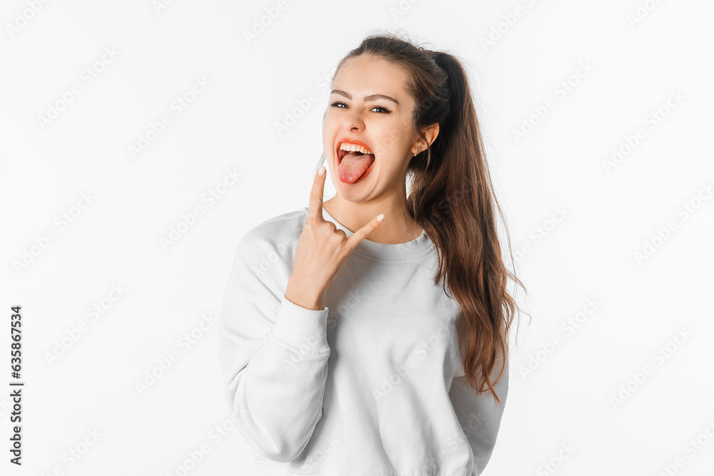 Crazy young woman showing tongue and rock and roll hand gesture, depicting heavy metal rock sign, posing in studio on white background Crazy young woman showing tongue and rock and roll hand gesture, depicting heavy metal rock sign, posing in studio on white background