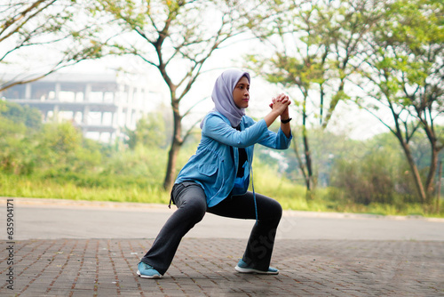 Beautiful Muslim woman working out outdoors in the morning. Sporty woman with a hijab warming up by doing exercises.