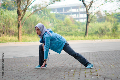 Beautiful Muslim woman working out outdoors in the morning. Sporty woman with a hijab warming up by doing exercises. photo