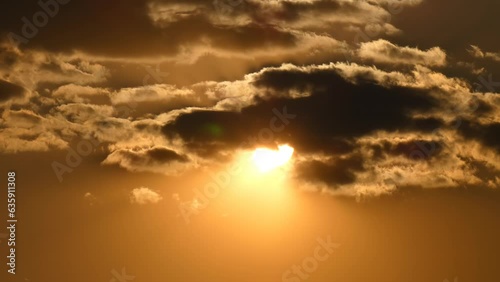 Sun passes through dramatic gray clouds on a golden sky during sunset photo