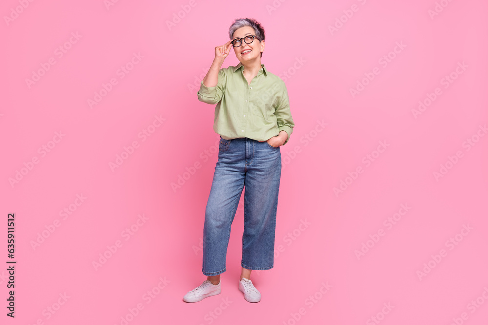 Full body photo of creative minded aged lady hand touch eyeglasses look empty space ad isolated on pink color background Full body photo of creative minded aged lady hand touch eyeglasses look empty space ad isolated on pink color background
